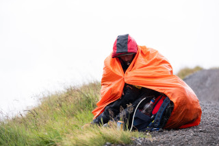 A volunteer at a downhill event, sat inside a bright orange survival bag in the rain