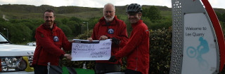 Chris Smith presenting the cheque to the team at the entrance to the quarry